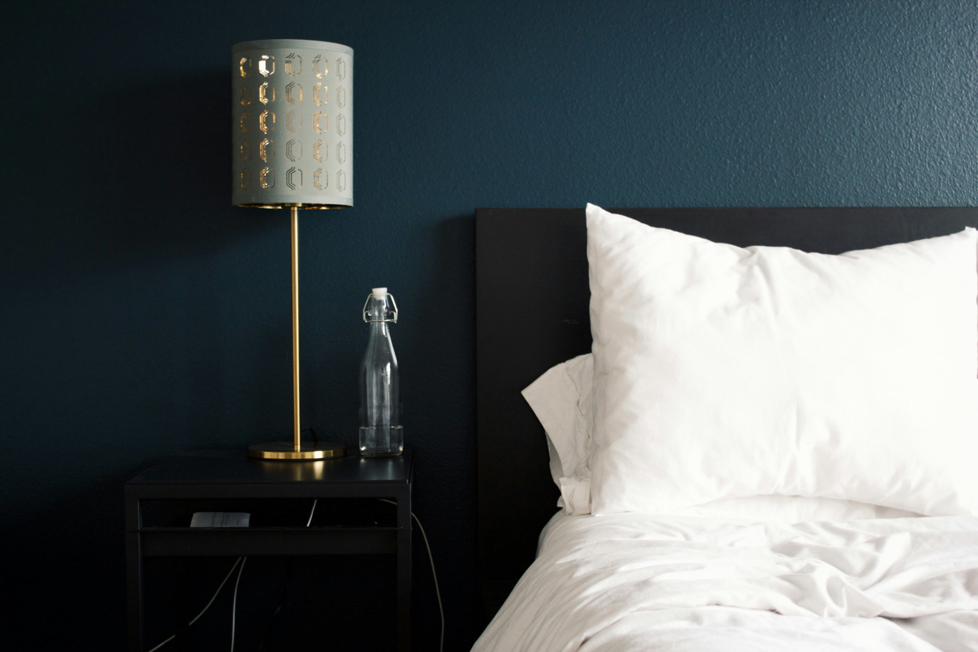 A neatly made white bed in a dark navy hostel room